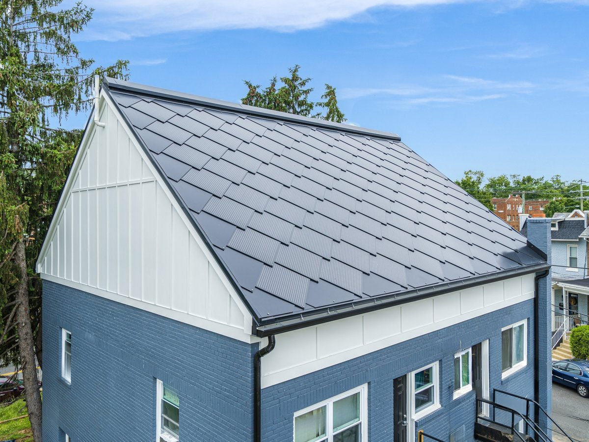 Flush-laid charcoal roof tiles with no visible mounting rails on a blue painted brick home